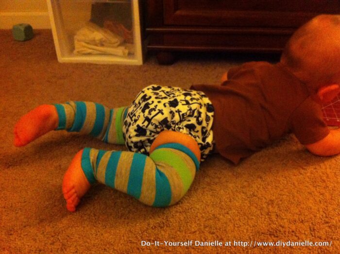 Baby leg warmers made with no sew method using hem tape. Baby is crawling on the floor with the leggings on and wearing a brown shirt and black and white cloth diaper.