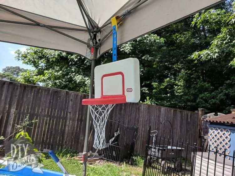 Basketball hoop in an above ground pool, hanging off the canopy being used for shade.