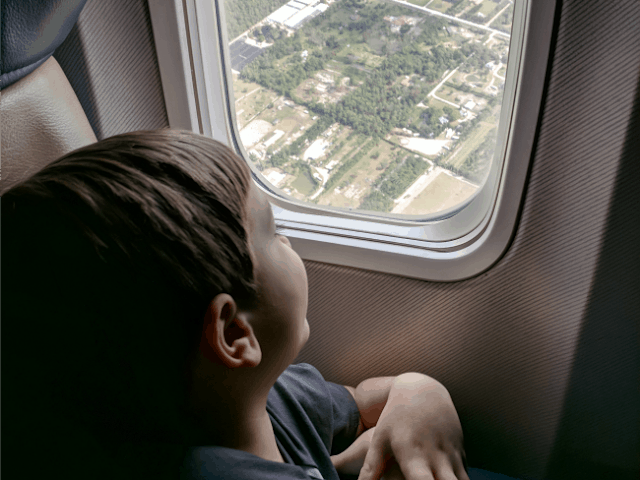 Child watching out the window on an airplane. Traveling with kids can be easy and fun for kids.