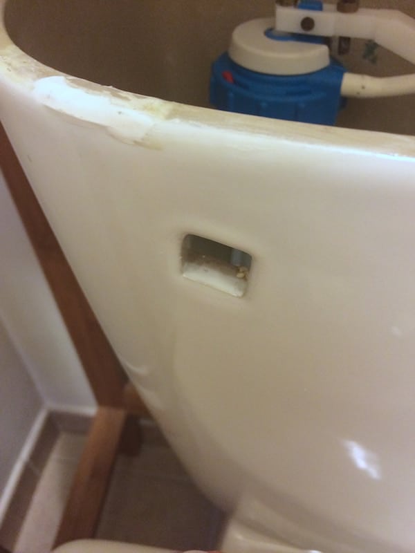 Toilet with the handle removed so the handle can be replaced. There is a small square gap. 