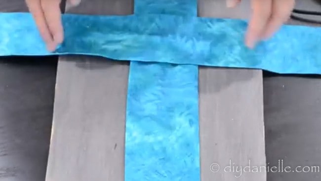 Second strip of fabric being placed over the first to create a cross on wood.