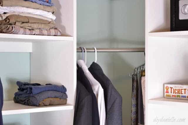 White closet shelves and a silver rod with clothes hanging. Shelves are plywood with veneer covering the raw edge.