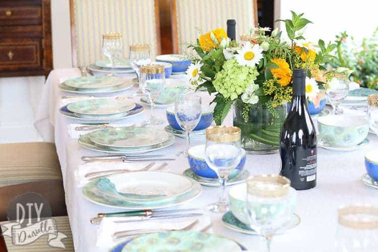 Peacock themed tablescape with a pop of color from the wine bottles and floral arrangement.