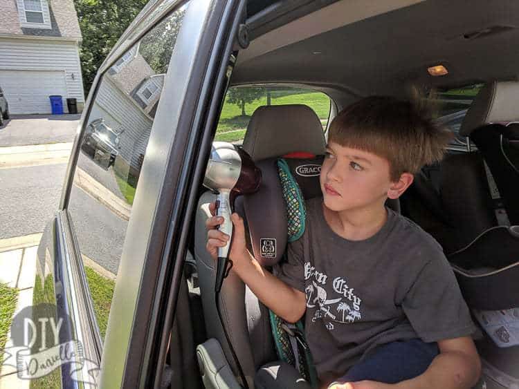 Six year old helping clean stickers off the car windows with a hair dryer.