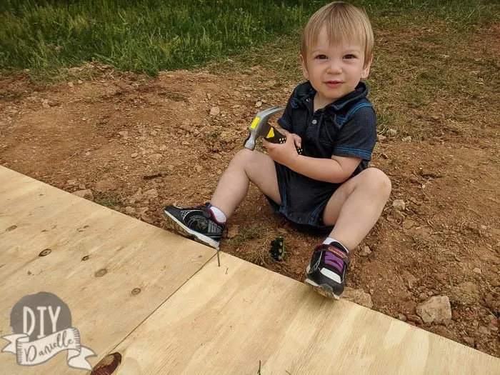 Toddler hammering nails into the plywood for the shed base.