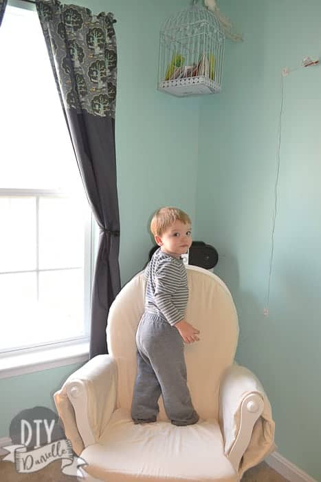 Little boy standing on the newly reupholstered rocking chair, next to the blackout curtains.