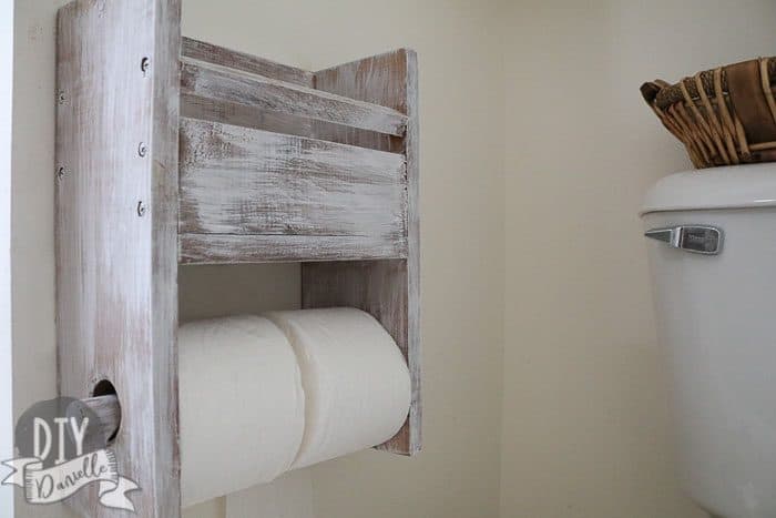 Rustic toilet paper holder that has two rolls plus room for a small book or magazine above it.