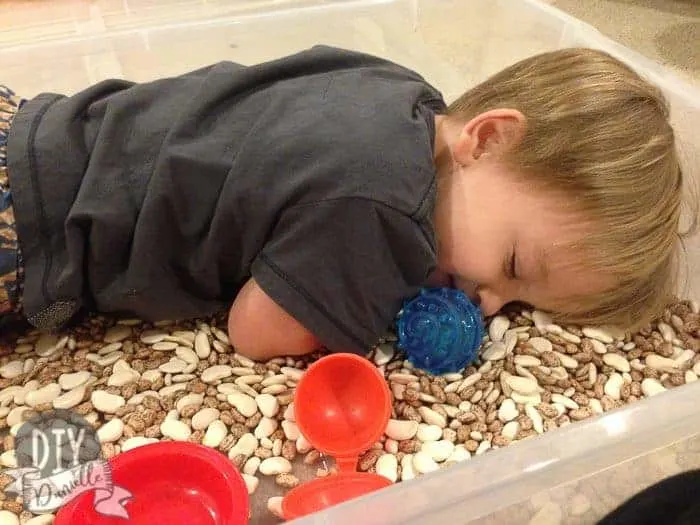 Son laying in a bean sensory bin.