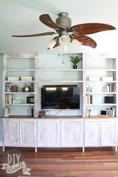 Photo of the bookshelves and cabinets from the front. The finish matches well with the flooring and ceiling fan.