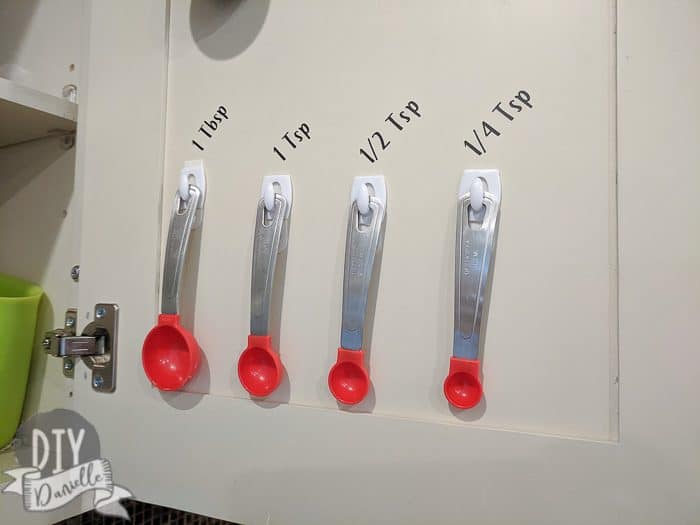 Measuring spoons hanging inside a cabinet and labeled by size.