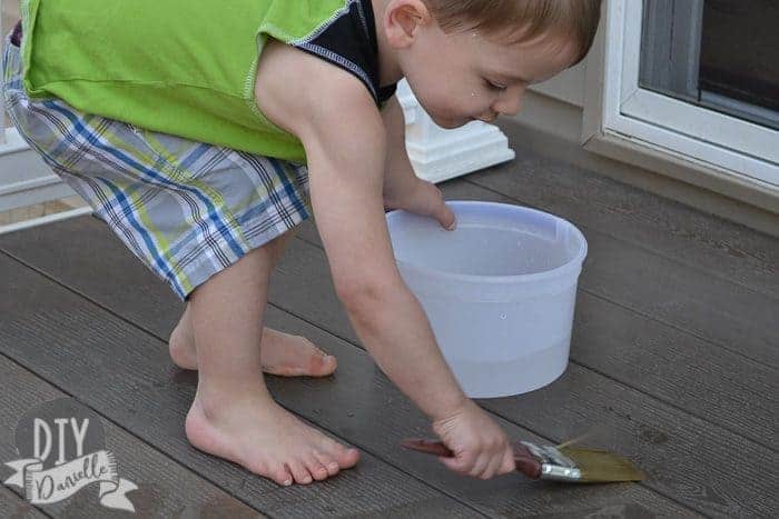 Boy painting the deck with paintbrush with water on it.