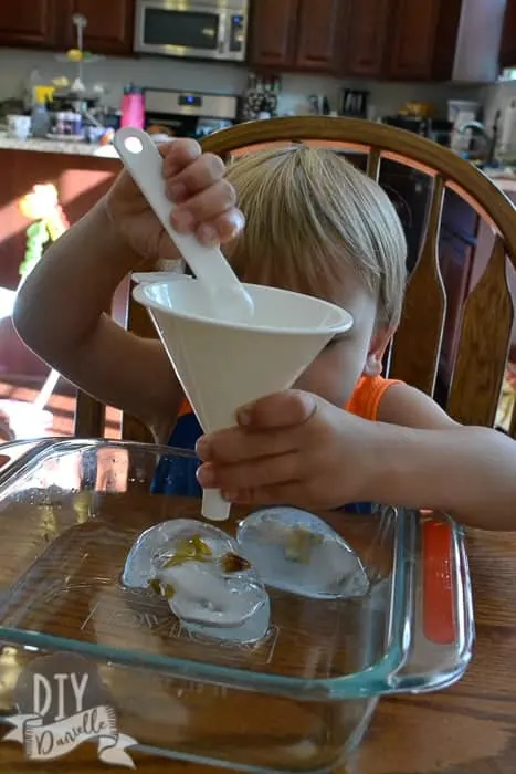 Toddler using a funnel and a measuring spoon to melt ice. 
