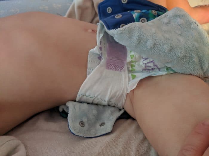 Disposable on my toddler. Starting to put the cloth diaper cover over the disposable. 