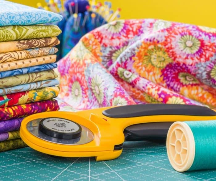 Photo of an orange rotary cutter next to thread and fabric. 