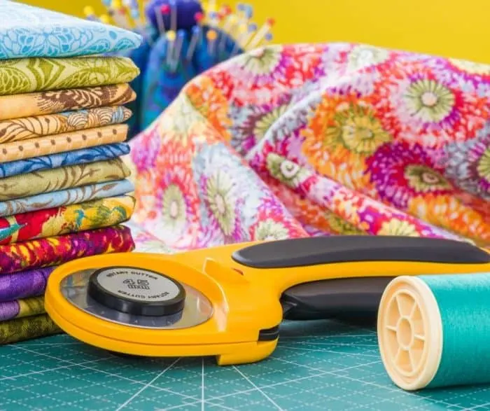 Photo of an orange rotary cutter next to thread and fabric.