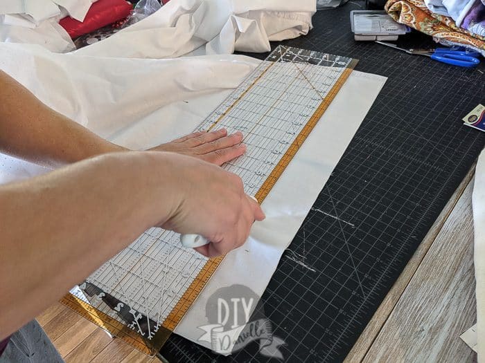 Using a rotary cutter to cut strips of white fabric. Also pictured: self healing cutting mat and quilting ruler.