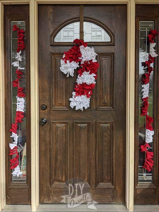 Twine and fabric banners on windows framing the wood door. Candy cane wreath on door.