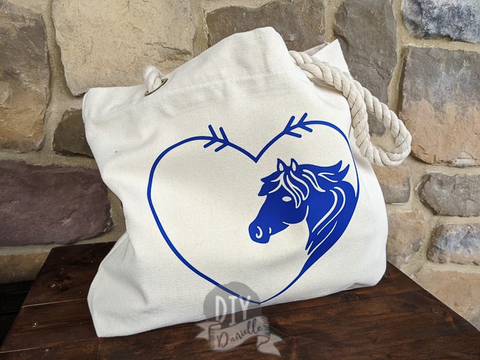 Outside of the canvas tote bag with rope handles. The iron on design is purple with a heart around a horse's head.