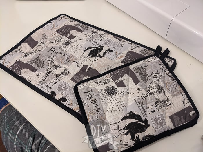 Double Fold Black bias tape around two pot holders with farmhouse fabric (farm animals on it). 