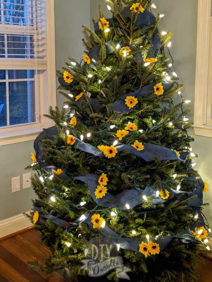 White lights on Christmas tree with sunflowers and blue burlap. 