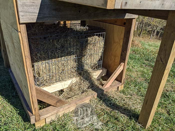 Dog crate under the goat playground, a bale of hay inside.