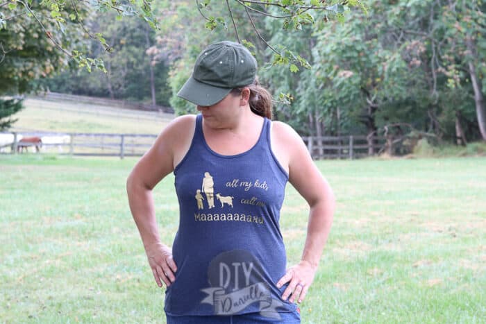"all of my kids call my maaaa" shirt on a woman in a purple tank with horses in field behind.
