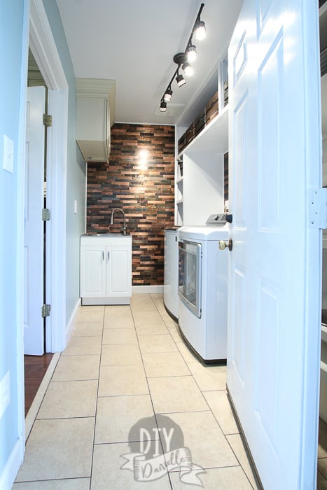 Laundry/mudroom with custom white plywood shelving, a small white sink, and metallic backsplash wall. The door to room is open.