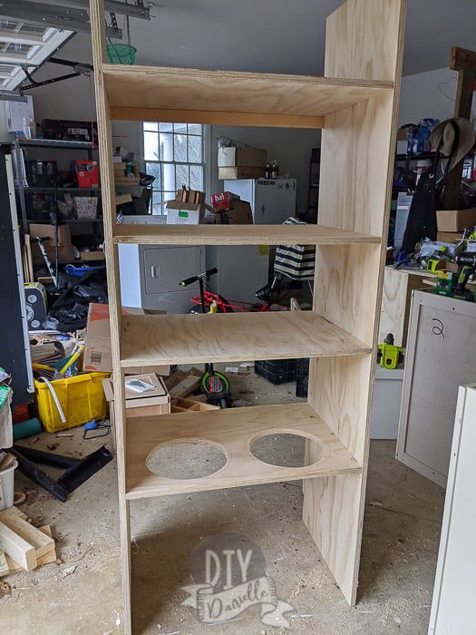 Large pantry shelf built from plywood. Not painted yet. A shelf at the bottom has cut outs for two metal dog bowls.