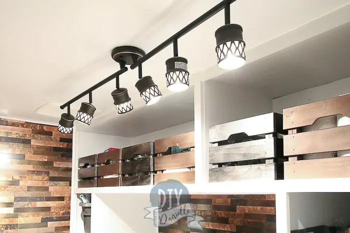 Rubbed bronze track lighting for laundry room adds a lot of light. Storage bins painted metallic colors on the top mudroom shelves.