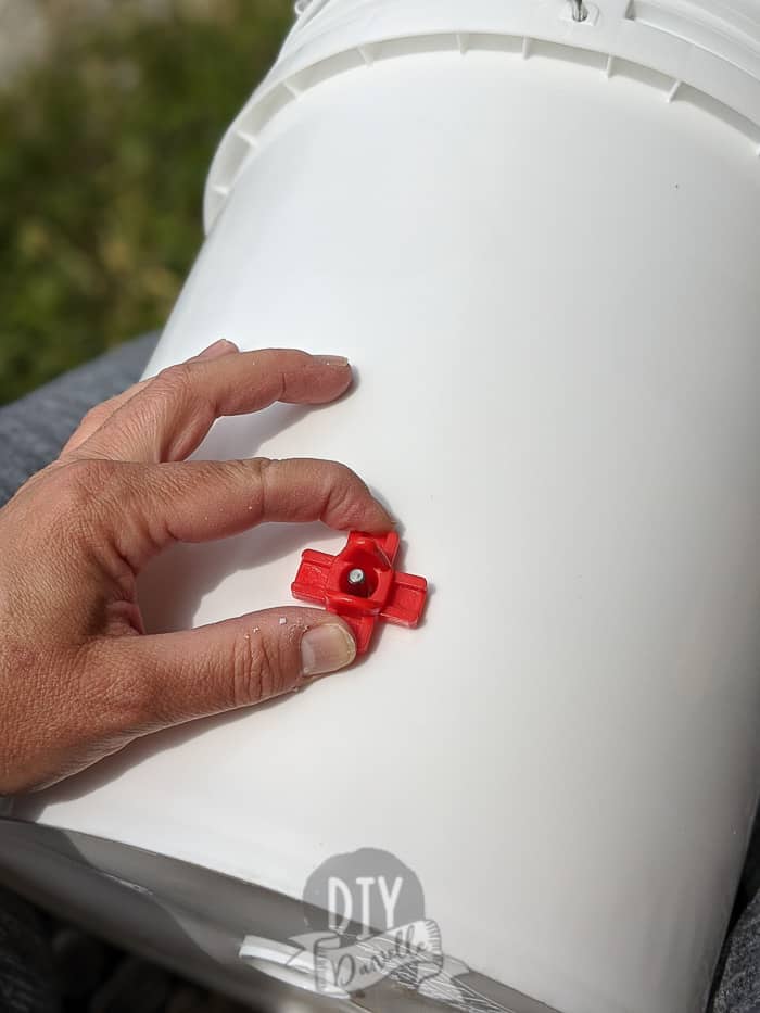 Screwing in a red nipple waterer into a white bucket.