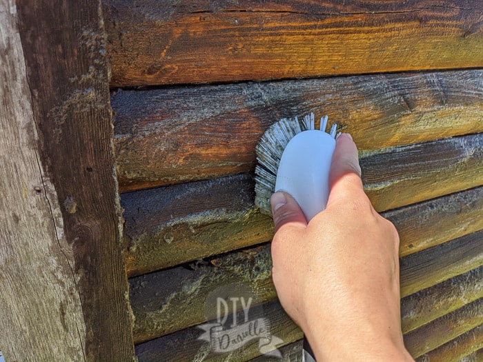Using a scrub brush and DIY wood cleaner to get dirt and debris off the old wood of this log cabin playhouse.