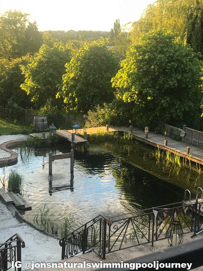 Completed DIY swimming pond with a shallow section around the perimeter for plants, lighting, wood dock, and more.