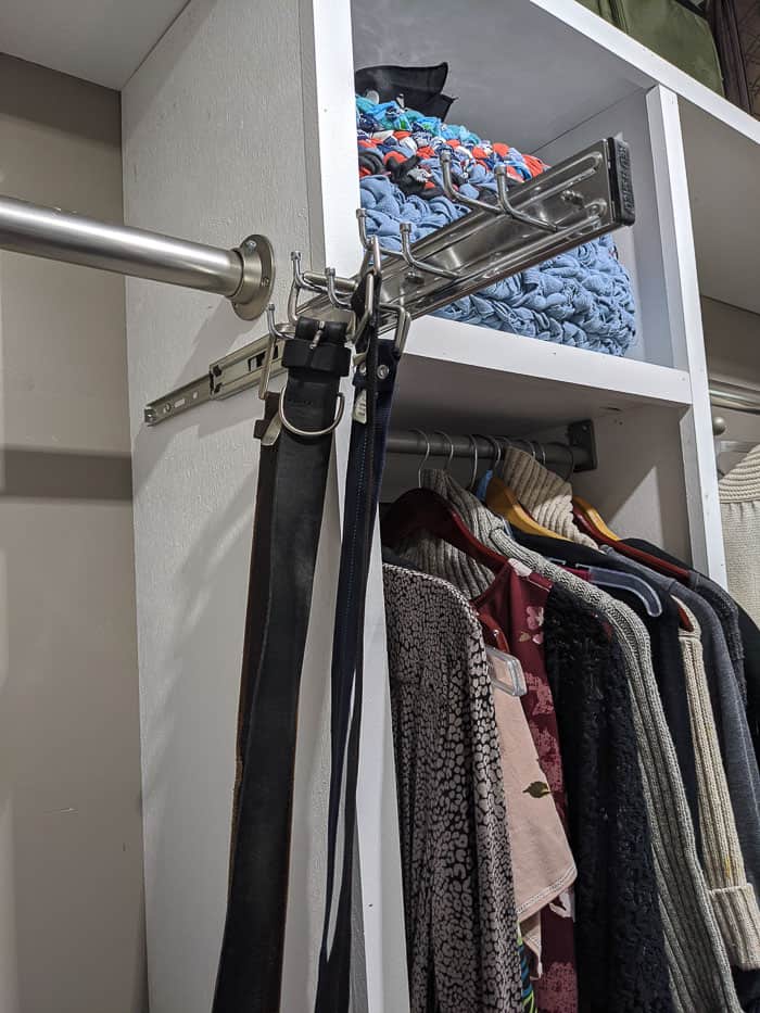 Silver/Chrome Belt rack that slides out from closet. It needs to be screwed into wood shelving or the wall. Four belts hanging from it. 