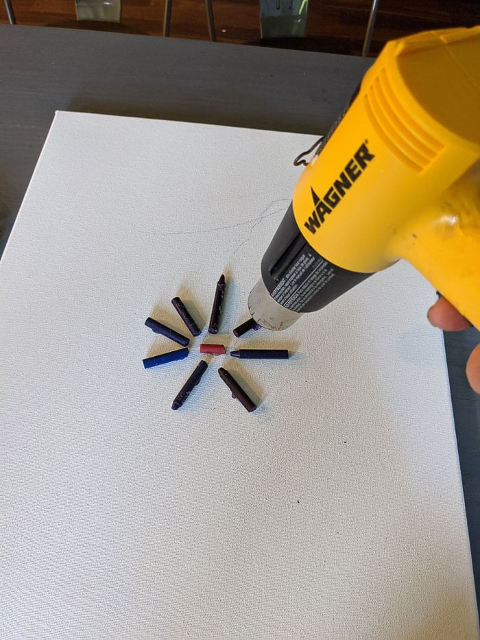 Using a Wagner Heat Gun to melt the crayons that have been glued to the canvas.