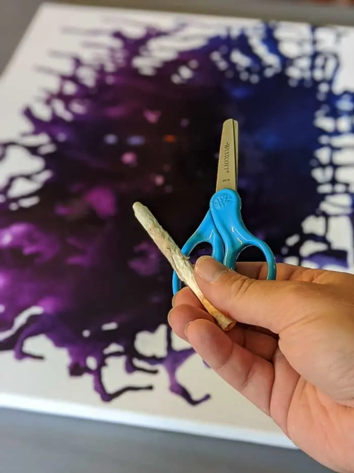 Kids scissors and white crayon with canvas art in background.