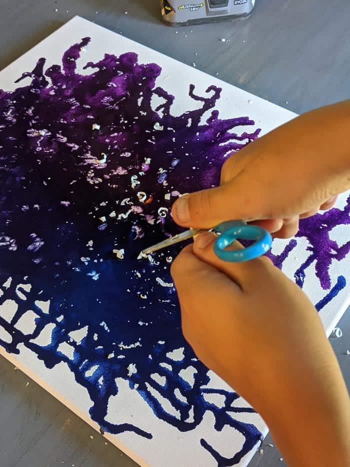 Using scissors to shave pieces of white crayon off onto the canvas.