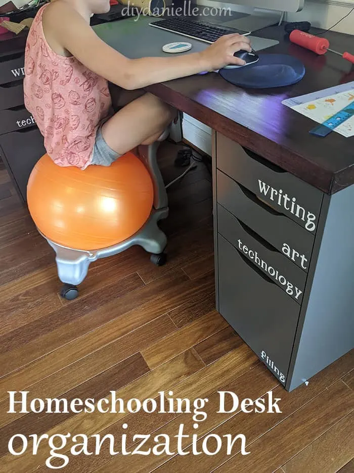 Young boy sitting on a bounce chair while he works on a computer for digital learning. The desk drawers are organized with the labels: Writing, Art, Technology, and Filing.