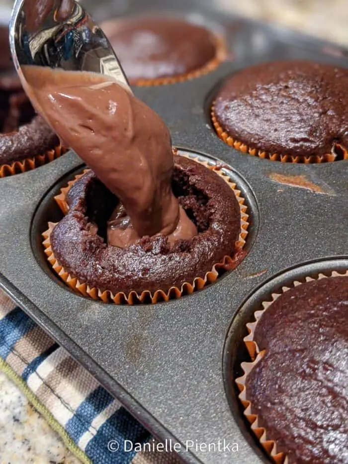 Putting a spoonful of pudding inside a cupcake.