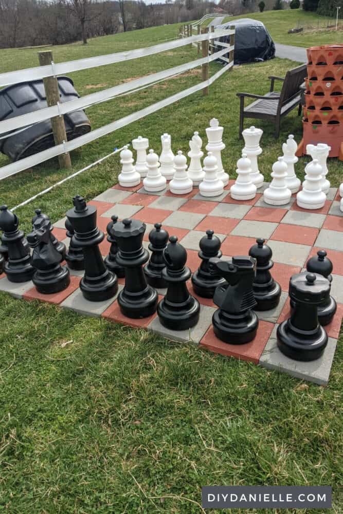 Giant chess board next to a field, a bench, and a garden tower.