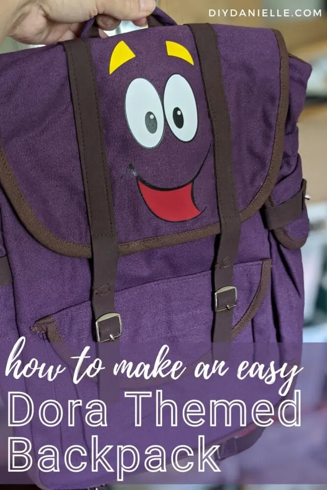 How to make an Easy Dora Themed Backpack. Purple backpack with a cartoon face heat pressed onto the front flap.