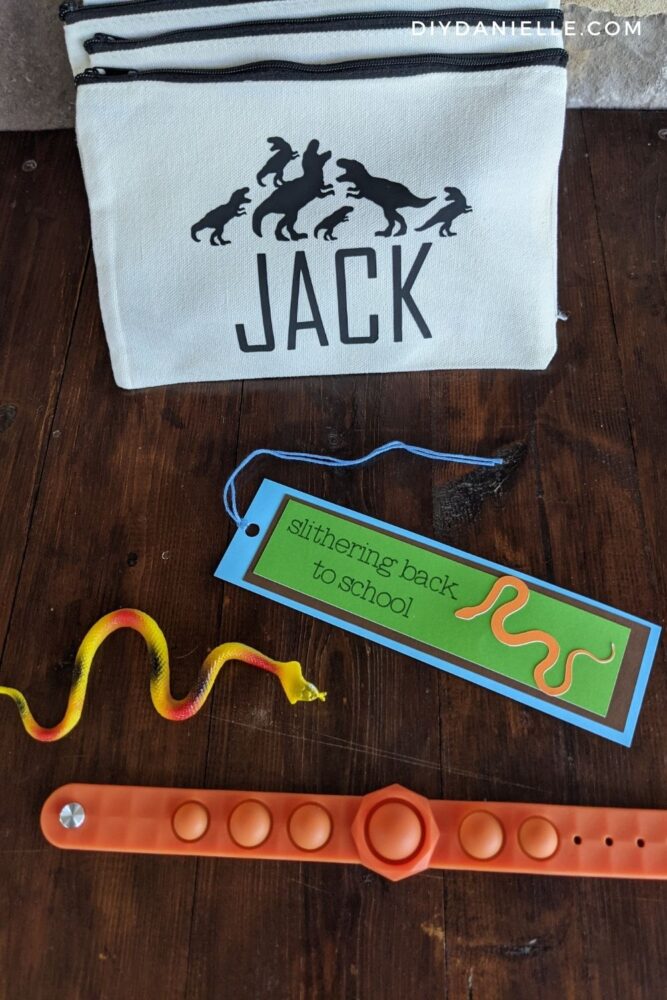 Set of items given as party favors for a boy's birthday party: "Slithering Back to School" DIY Bookmark, toy snake, a pop it bracelet, and a bag with the child's name and some dinosaurs on it. I also included a cloth mask, not pictured.