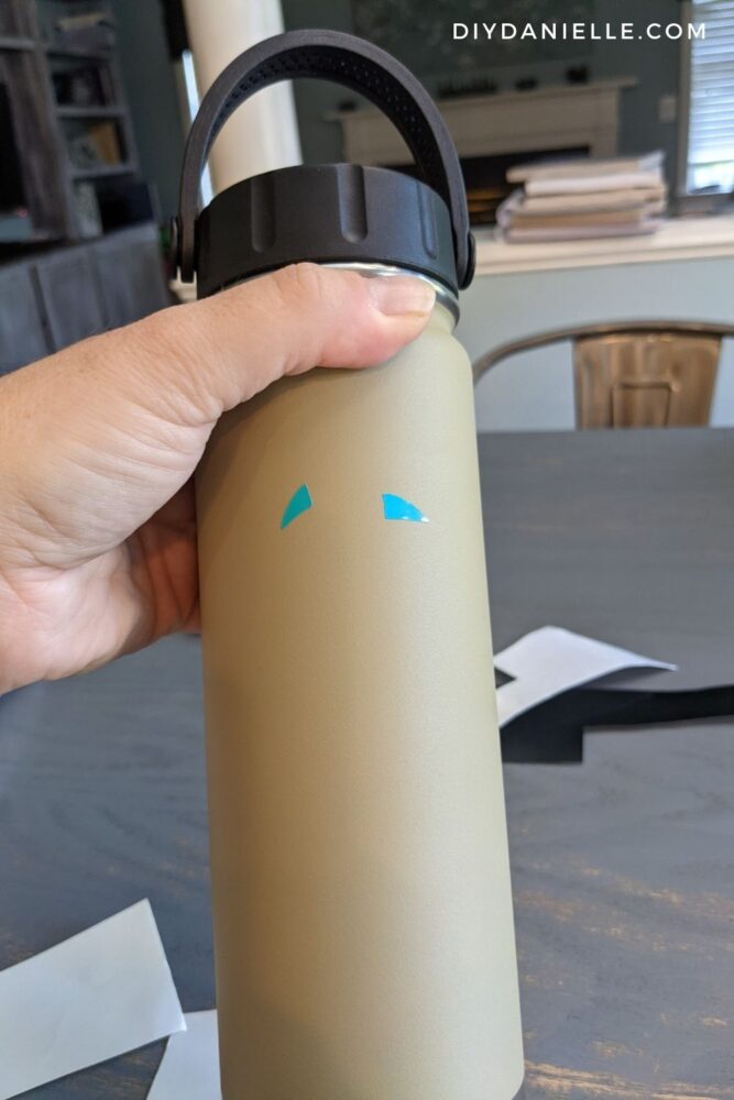 Tan water bottle with turquoise eyebrows added to it in vinyl.