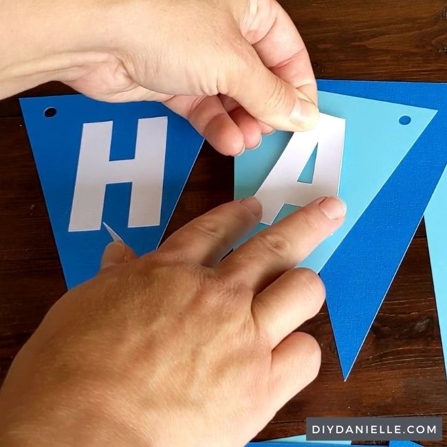 White letters being peeled off Smart Sticker Cardstock, then adhered to light and dark blue banner triangles.