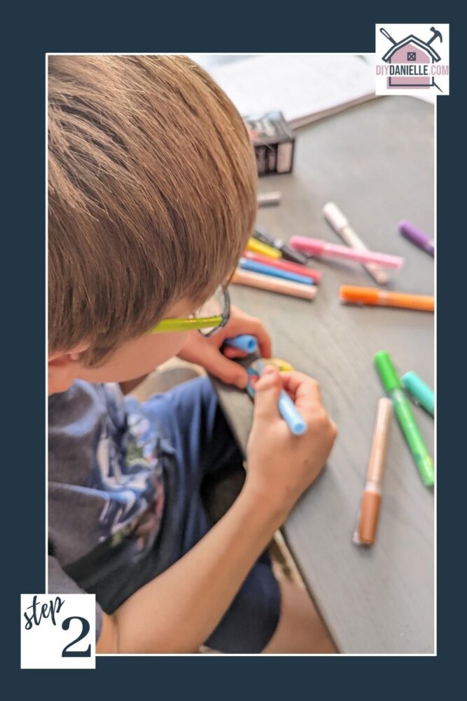 Blond child using acrylic paint markers to draw on a wood slice.