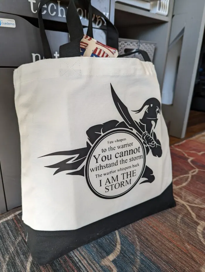 Large bag stuffed with items to help with chemotherapy with a quote "Fate whispers to the warrior 'You cannot withstand the storm.' The warrior whispers back, 'I am the storm.'" 