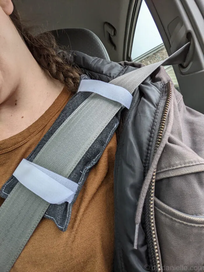 Me, demonstrating the position of the port pillow on the seat belt while the patient is in the car. The port pillow is up against their clothing with the hook and loop on the opposite side.