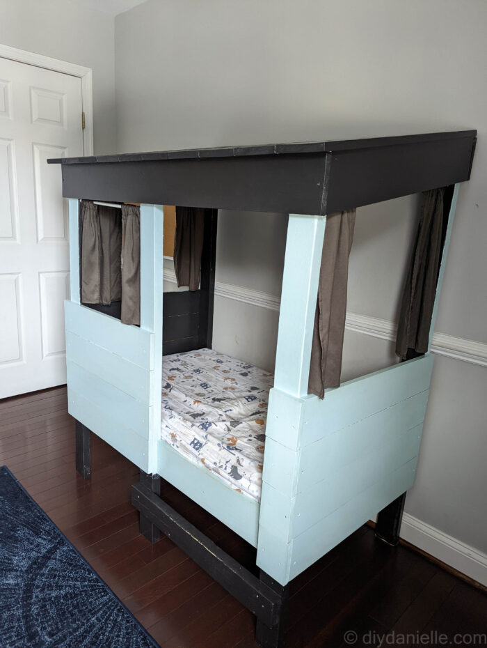 Finished DIY Toddler Bed with black roof, gray curtains, and light blue sides.