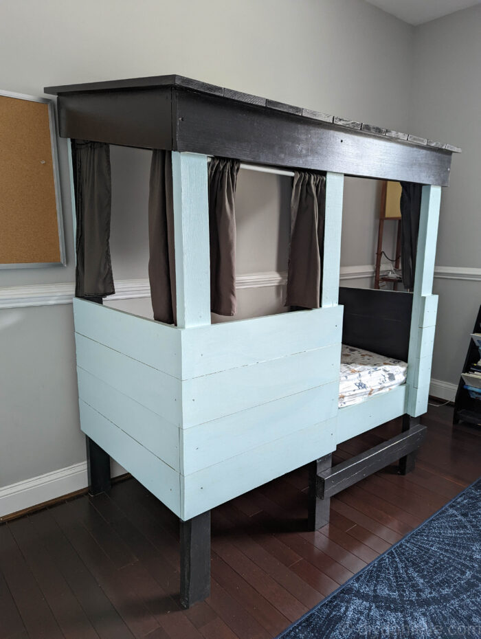 Finished DIY Toddler Bed with black roof, gray curtains, and light blue sides.