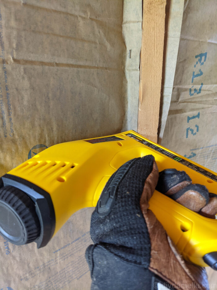 Photo of insulation being stapled to the side of a stud using a yellow and black staple gun.
