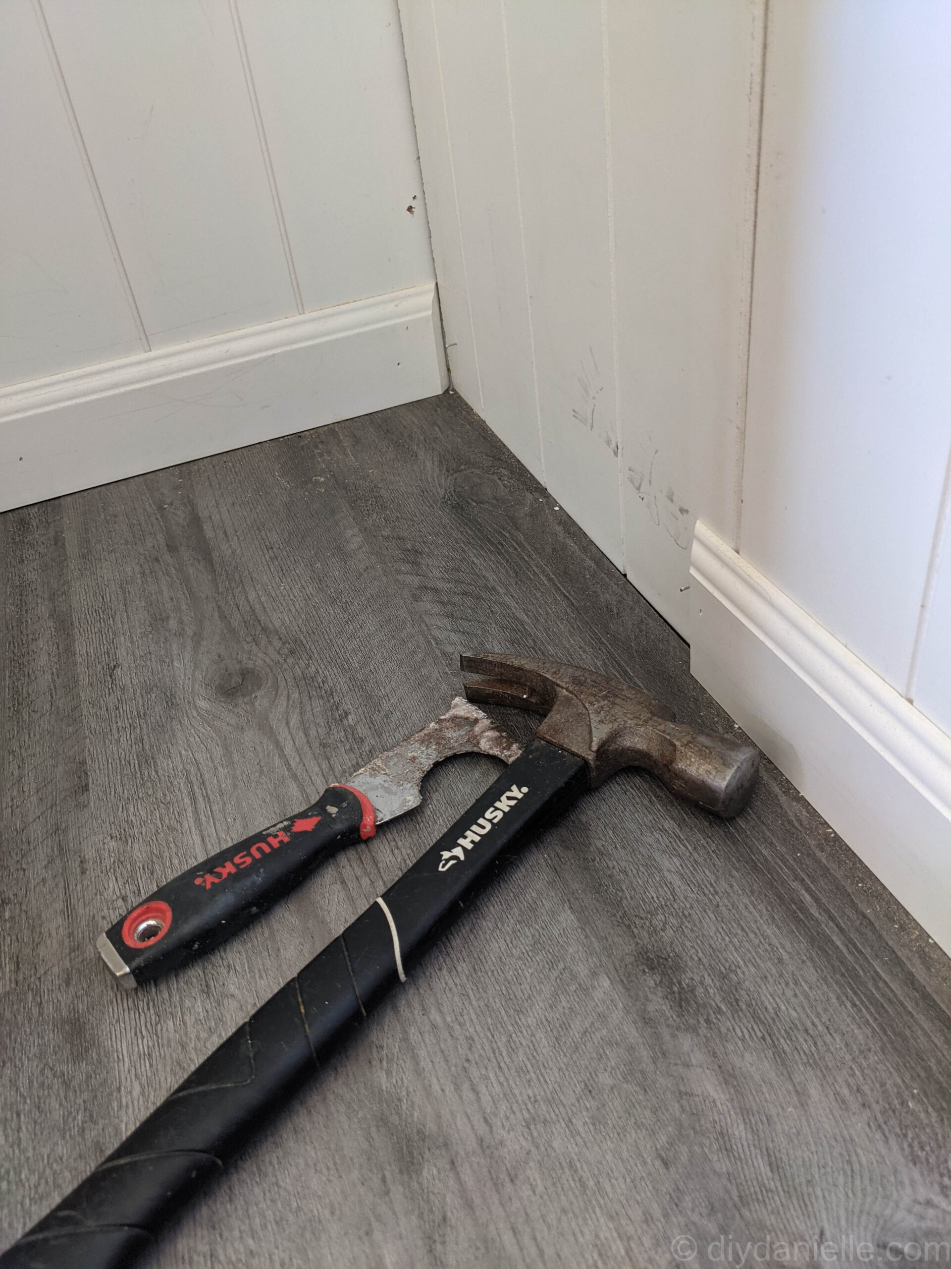 Cutting vinyl plank flooring with a jigsaw to fit around an uneven bathroom entrance before installing baseboards.